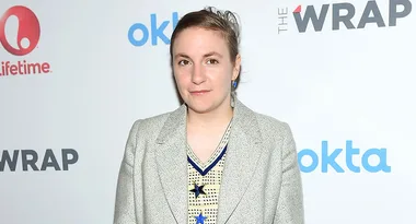 A person in a gray blazer poses at an event with logos for Lifetime, The Wrap, and Okta in the background.