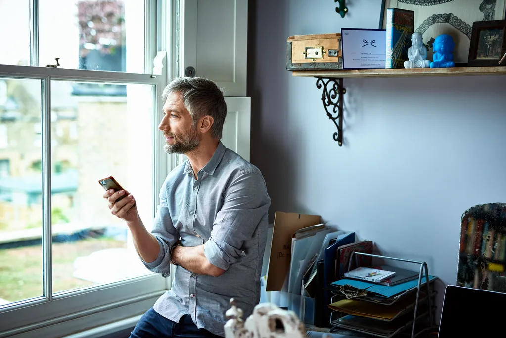 Man looking out window holding an iPhone