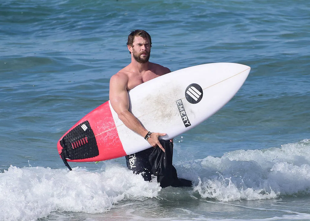 Chris Hemsworth holding a surfboard at the beach