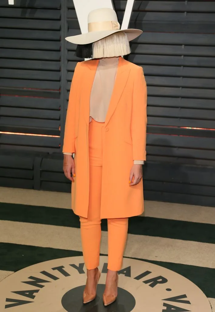 Sia in an orange suit outfit with a white hat, at the 2017 Vanity Fair Oscar Party