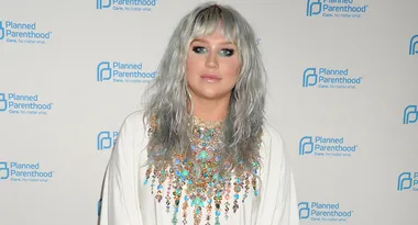 Silvery-haired woman in a colorful embellished outfit at a Planned Parenthood event backdrop.