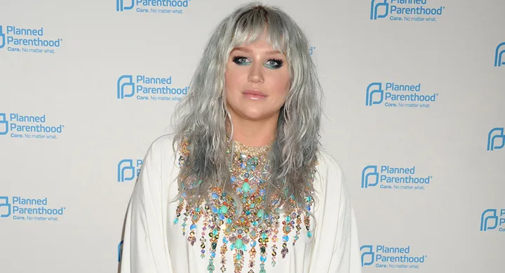 Silvery-haired woman in a colorful embellished outfit at a Planned Parenthood event backdrop.
