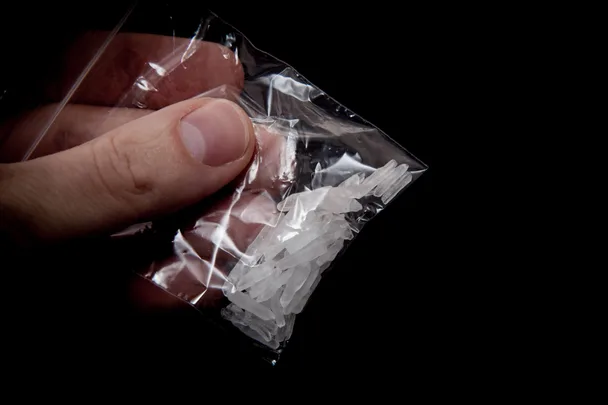 Hand holding small bag of methamphetamine against black background
