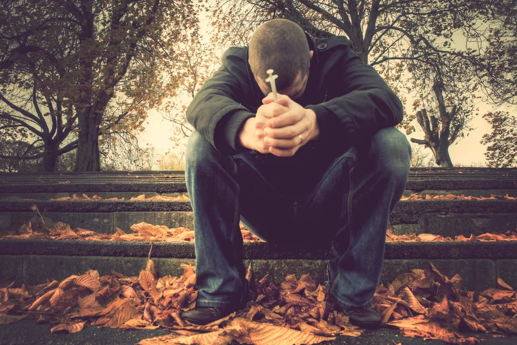 Man sitting on steps with head in his arms holding needle