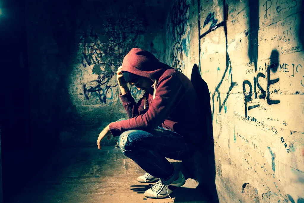 Man sitting in dark tunnel with a red hoodie and blue jeans