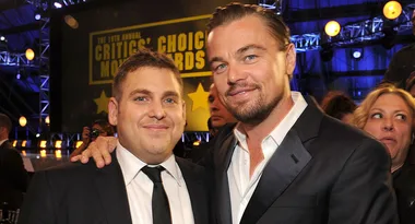 Two men in suits smiling at the Critics' Choice Movie Awards with a crowd and stage in the background.