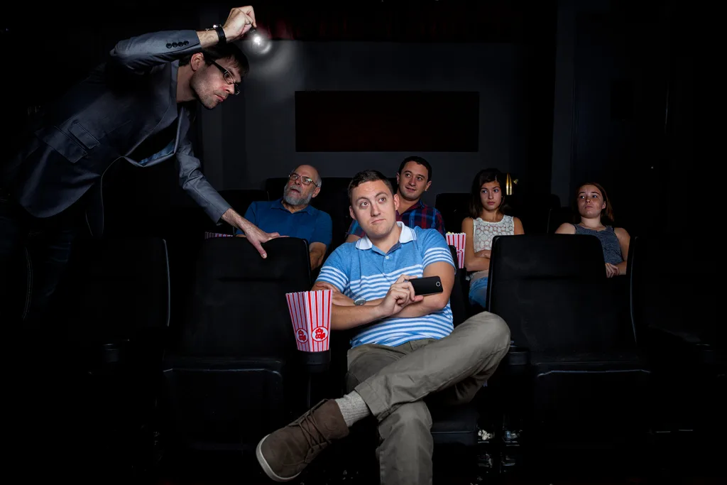 Man watching movie in a cinema with a security guard shining torch on him