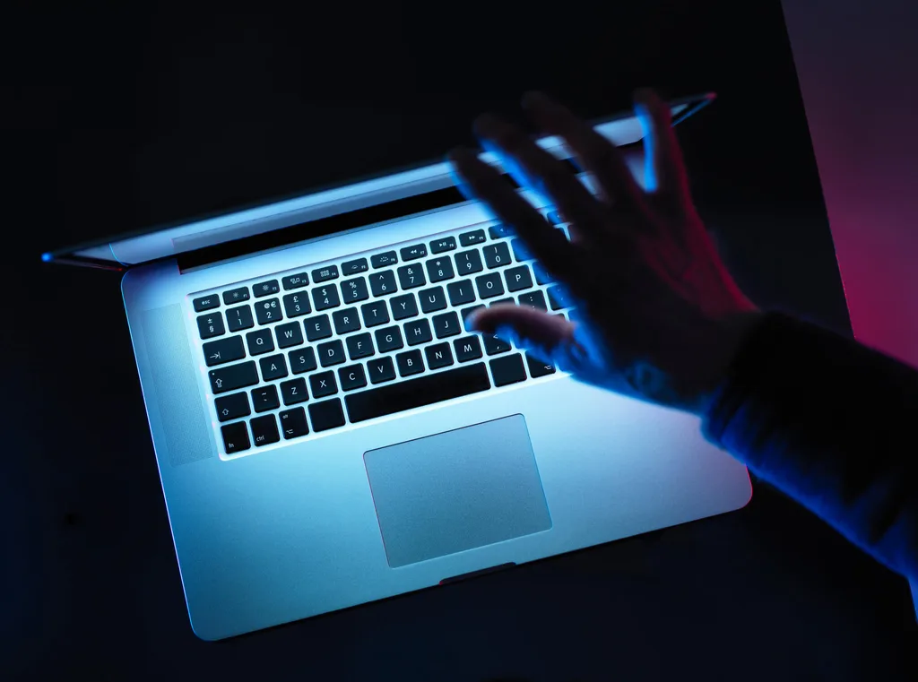 A man's hand covering a Apple Macbook screen in the dark