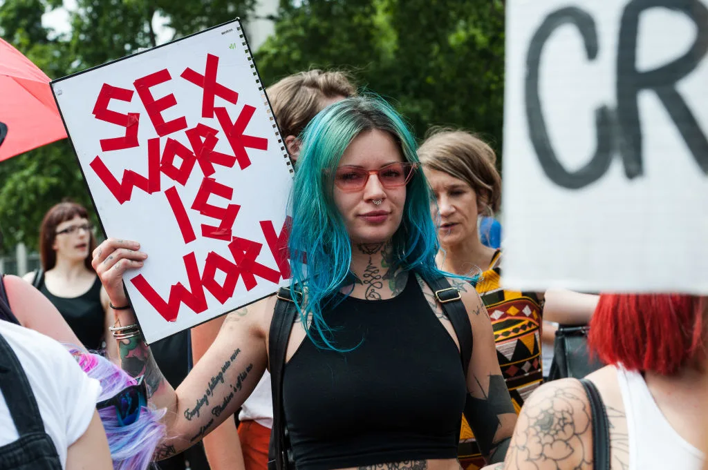 Sex worker protesting with a sign that says 'sex work is work'