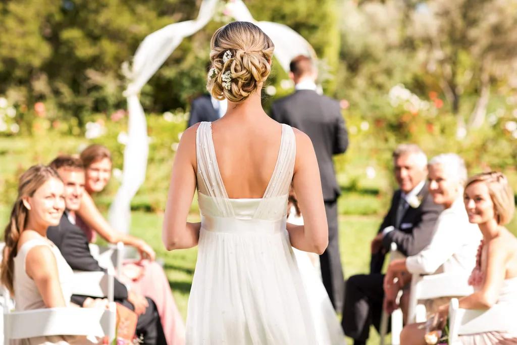 A bride in a white dress walking down the aisle at a wedding cereomy