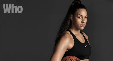 Basketball player in a black sports bra holding a basketball against a dark background.