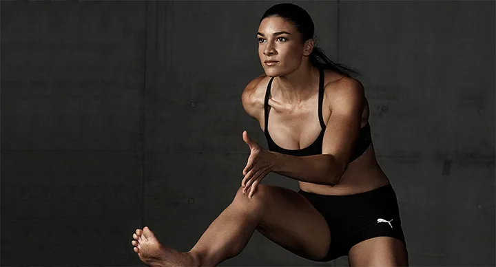 Woman in athletic pose wearing black Puma sportswear, set against a dark background.