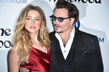 Two people posing at a formal event, one in a red dress and the other in a suit and sunglasses.
