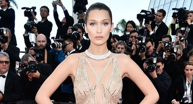 Celebrity in a glamorous gown poses on red carpet, surrounded by photographers taking pictures.