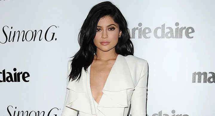Person in a white outfit posing in front of a Marie Claire backdrop.