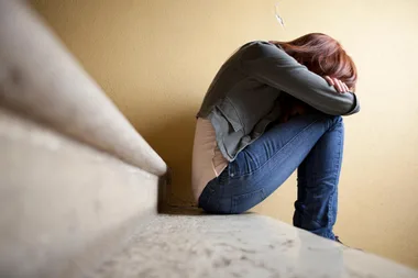 A young, depressed woman sitting on stairs with her head in her arms