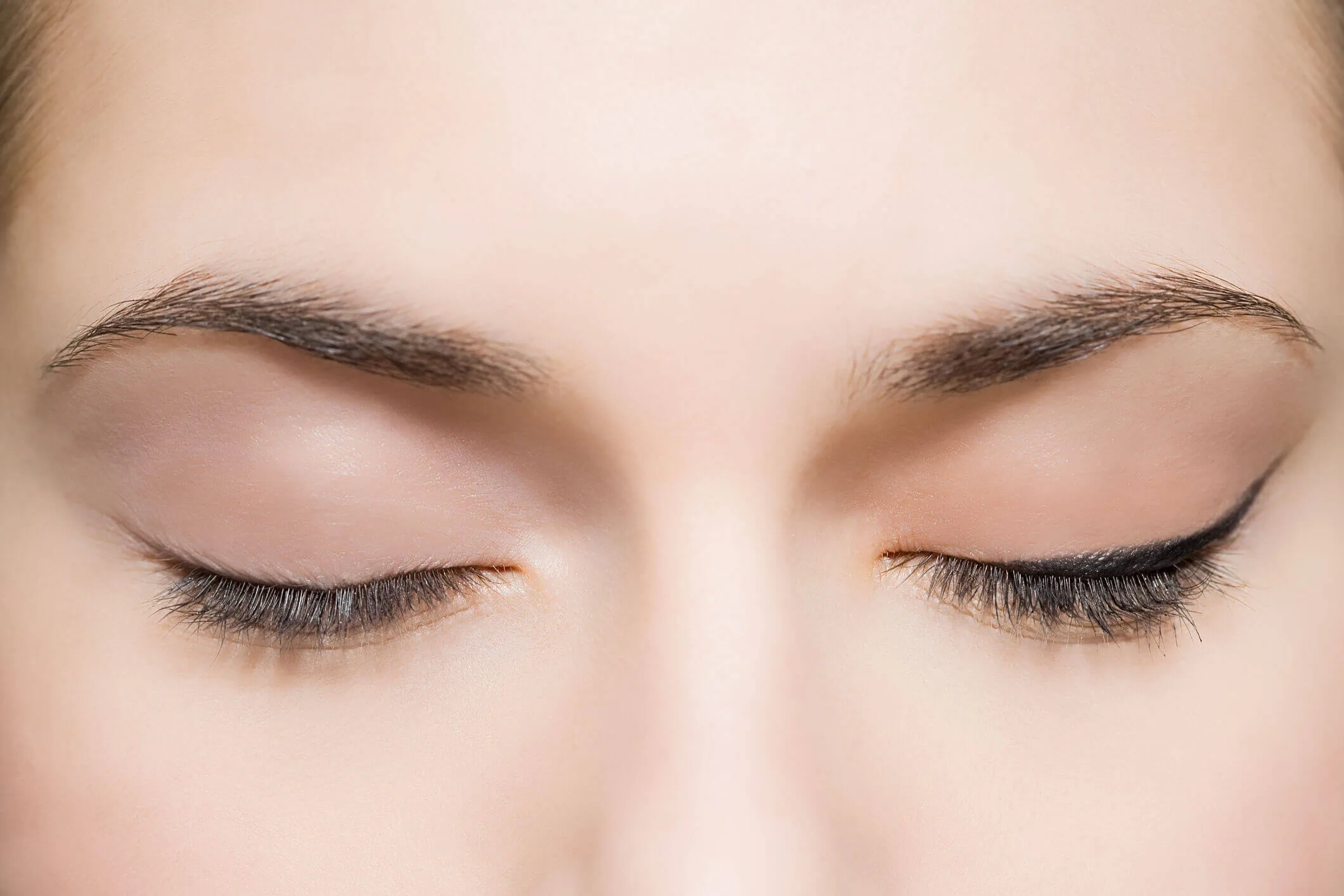 Close-up of a person's closed eyes with natural eyebrows and subtle eyeliner.