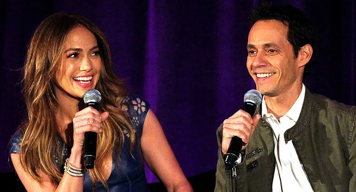 Two people smiling and holding microphones during a talk, seated in front of a dark purple curtain.