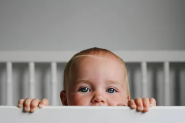 A baby looking over a bed frame