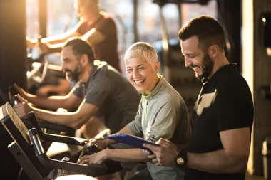 A male personal trainer standing next to a mature woman on a treadmill