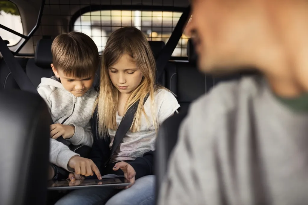 Two kids playing on an iPad at the back of a car