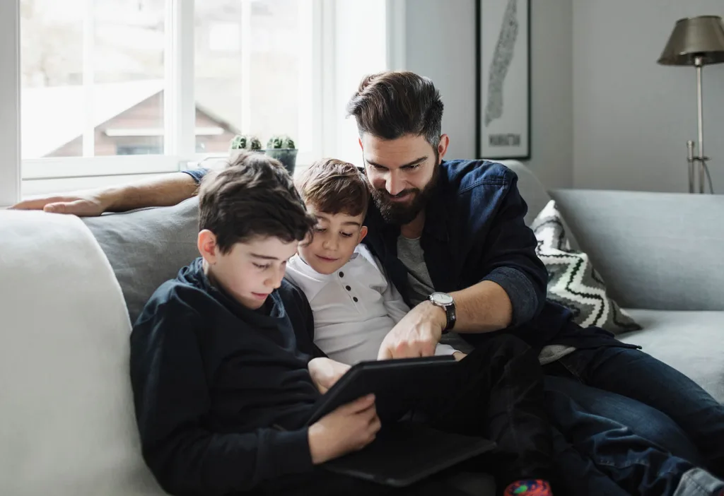 A dad and his two sons on a couch watching an iPad