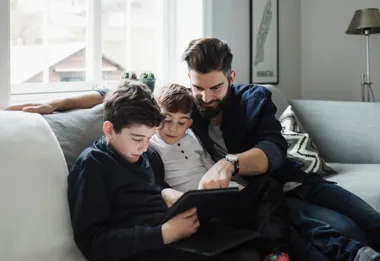 A dad and his two sons on a couch watching an iPad
