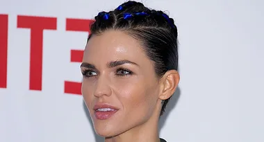 ```plaintext
Person with dark hair in braids, wearing a green top, in front of a blurred background.
```