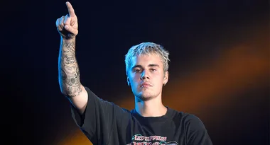 Singer with tattoos points upward, wearing a Led Zeppelin T-shirt, on stage with a spotlight backdrop.