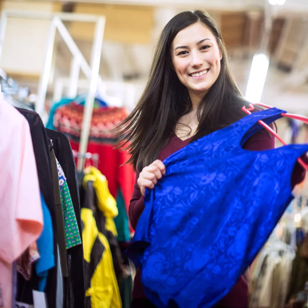 A woman holding up a blue top at a thrift store
