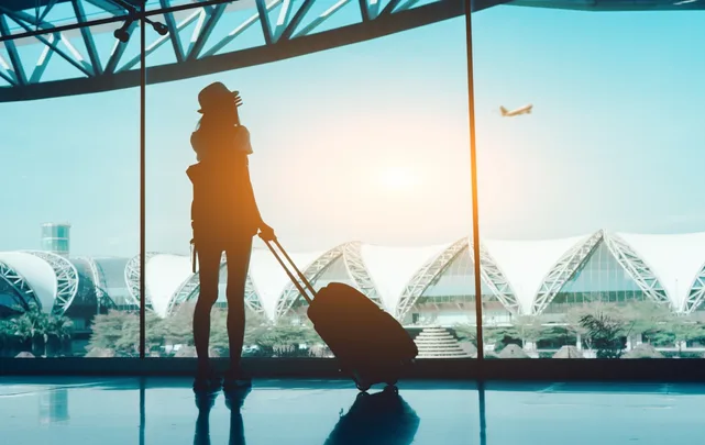 A young woman with a suitcase looking out of a window at an airport