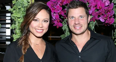 Couple smiling in front of vibrant pink flowers, both wearing black shirts, with greenery in the background.