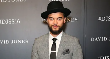 Man in a gray suit and black hat at a David Jones event with #DJSS16 background.