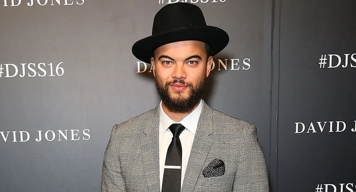 Man in a gray suit and black hat at a David Jones event with #DJSS16 background.
