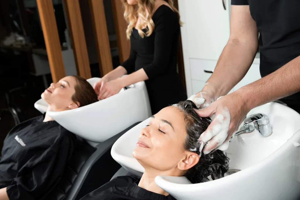 Two hairdressers washing the hair of two young women