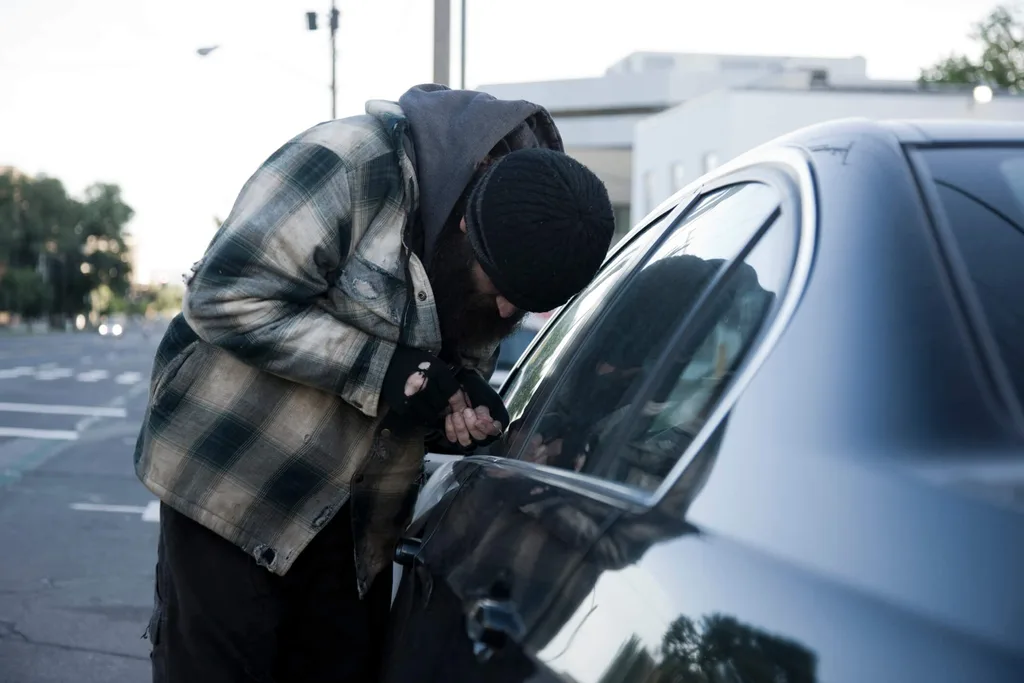 A man breaking into a dark coloured car