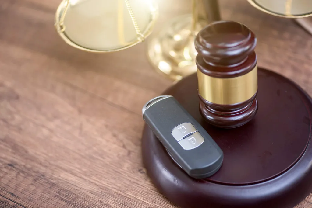 A gavel and car keys on a sounding block against a wooden table