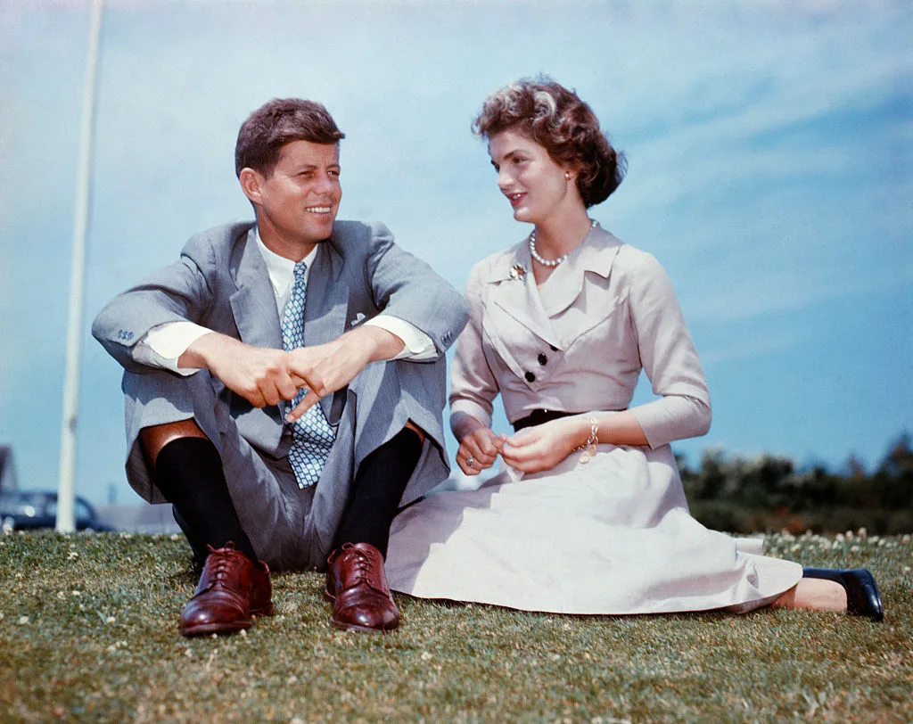 John And Jackie Kennedy sitting together on the grass outside the Kennedy family home