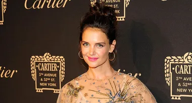 Person smiling at a Cartier event, wearing a detailed dress with gold and blue embellishments, elegant backdrop.