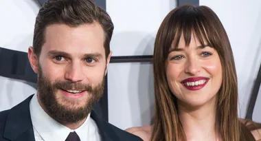 ```html
Alt text: "Man with a beard and woman with long hair smiling at a red carpet event."
```
