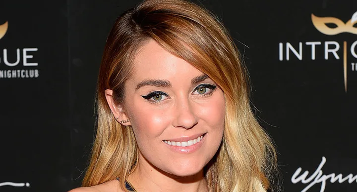 A woman with long blonde hair smiles at an event with a dark background featuring the word "Intrigue."