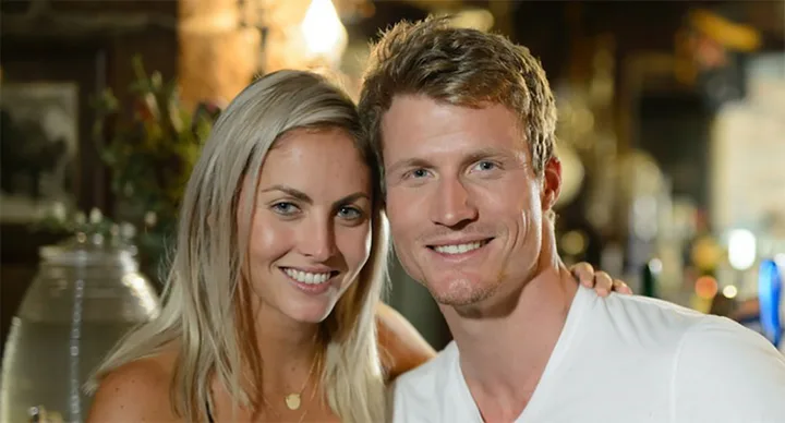 A smiling couple poses closely together in a warmly lit environment.