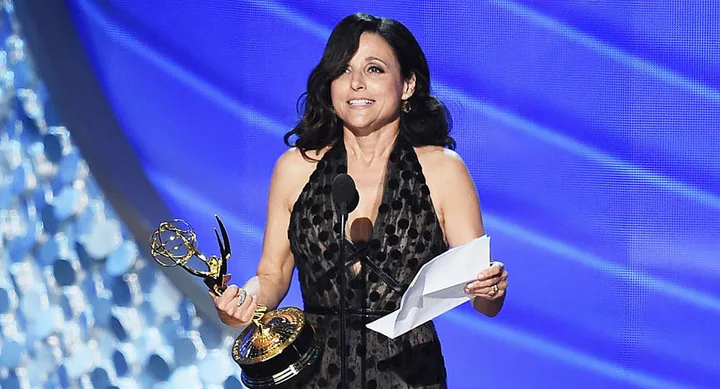 Winning an award on stage, wearing a black dress, with a backdrop featuring abstract blue patterns.