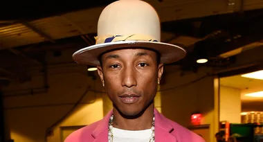 Man wearing a cream-colored hat and pink jacket in an indoor setting with dim lighting.
