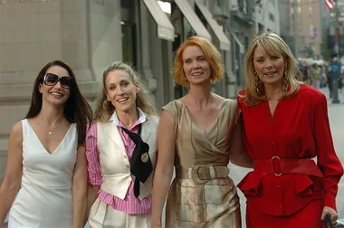 Four women walking together in stylish outfits on a city street.
