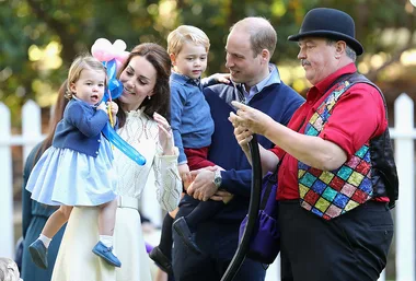 A family with two children enjoys a balloon artist's performance outdoors.