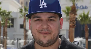 Person wearing a blue LA baseball cap outdoors with palm trees and buildings in the background.