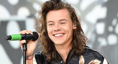 Singer with long hair smiling while holding a microphone on stage.