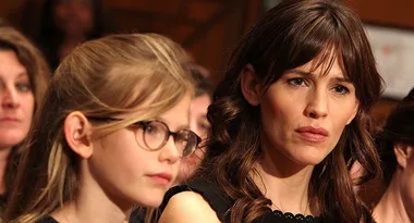 ```html
<img src="image.jpg" alt="A young girl with glasses and a woman with brown hair attentively listening in a crowd." />
```