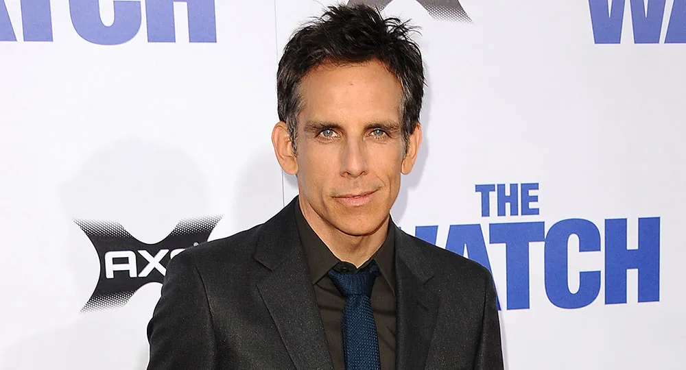 Man in a suit and tie at a "The Watch" movie premiere event backdrop.